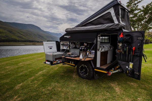 An Infanta 4x4 Enkulu 1 off-road caravan set up on green grass next to a lake